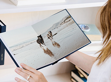 Woman holding photo book opened to two-page photo of dogs running on beach