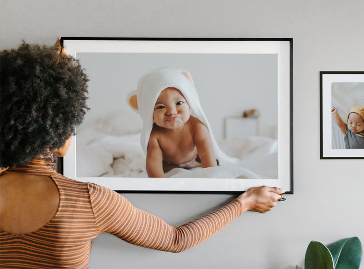 Woman hanging large framed baby photo in her new gallery wall