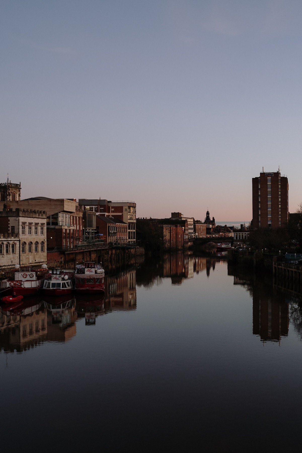 A body of water in a city with the reflections of the buildings shown on the water as the sun sets.