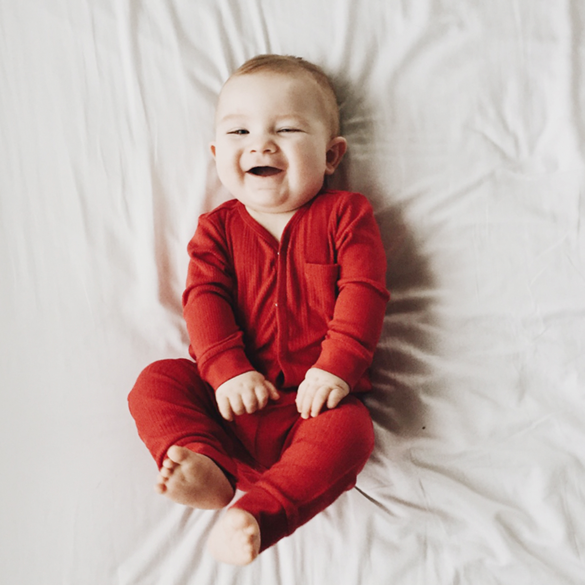 Baby in onesie laying on bed and laughing