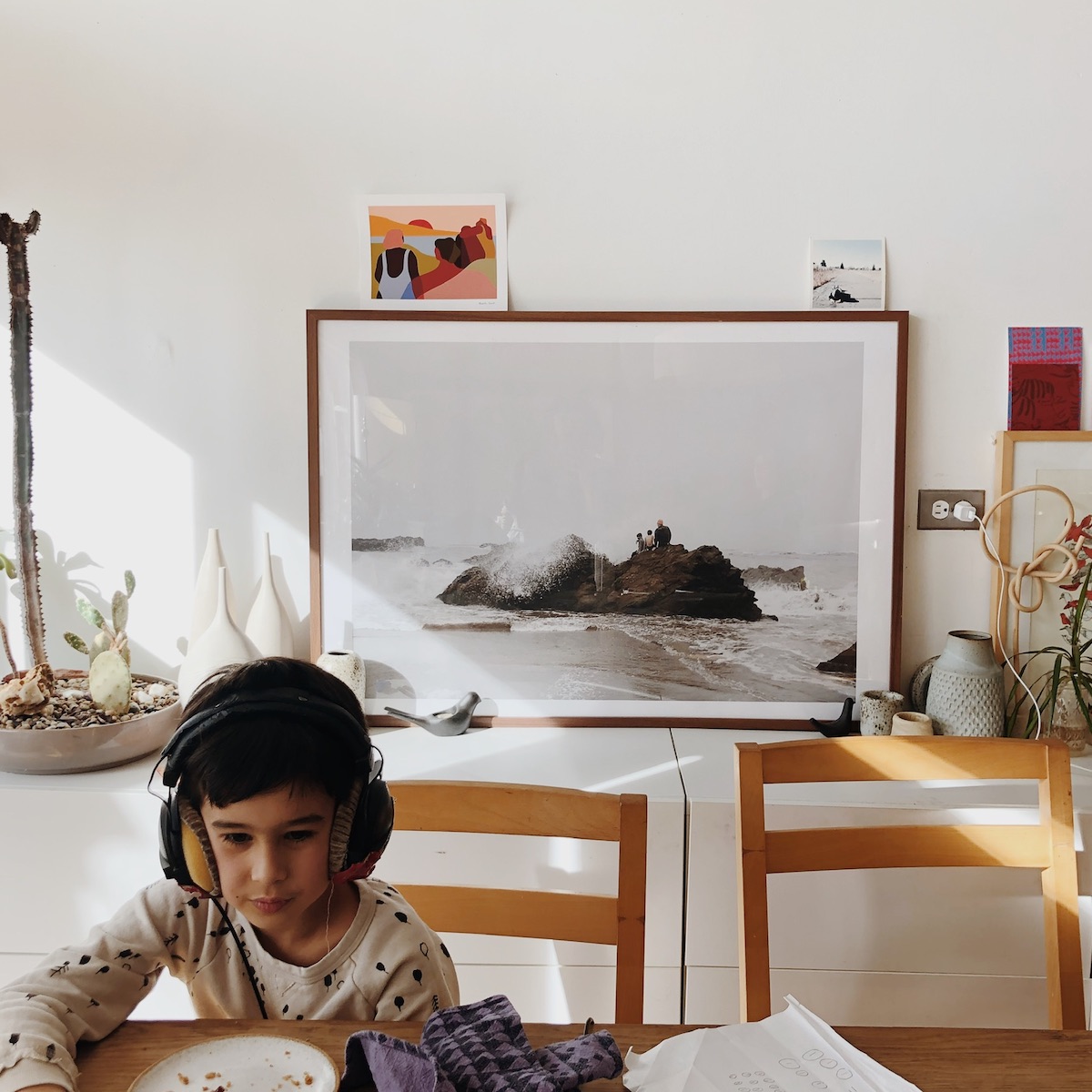 Little boy with headphones on at dining table with Artifact Uprising Large Format print of his family at the beach on credenza behind him
